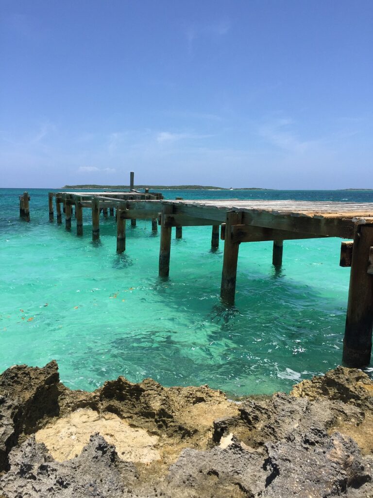 Wooden dock stretching into clear Bahamian waters with an island in the distance