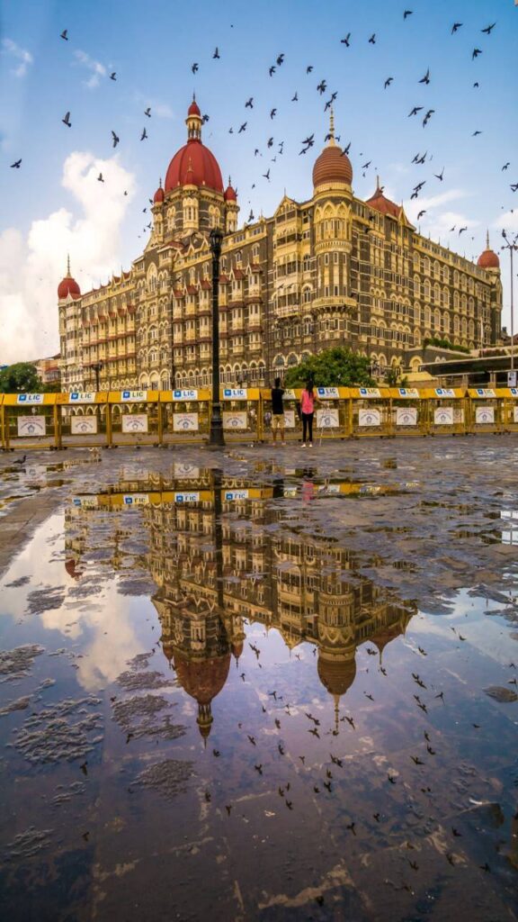 Taj Mahal Palace Hotel Mumbai reflected in rainwater with pigeons flying in the sky